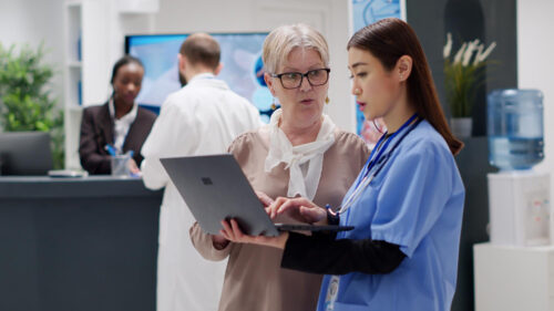 Healthcare staff reviewing information on a laptop at a hospital reception area.