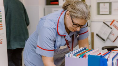 Nurse reviewing patient records in a clinical setting.