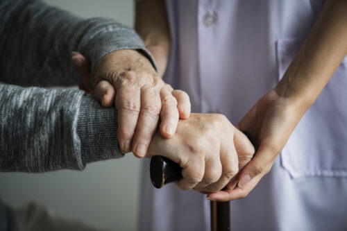 Close-up of a healthcare professional supporting an older person’s hands.