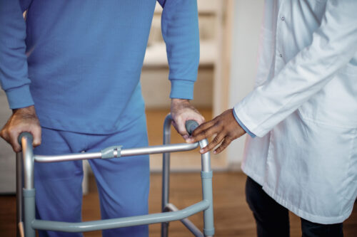 Person using a walking frame with support from a healthcare professional.
