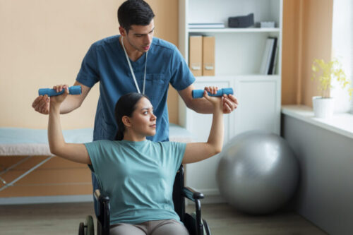 Person using light dumbbells during a rehabilitation exercise with support from a healthcare professional.